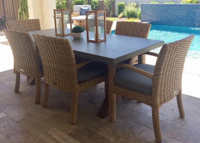 Wicker patio table on a decorative concrete patio, in front of an inground pool